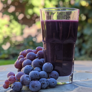 A pristine glass brimming with our vibrant dark purple grape juice, bursting with goodness and health benefits, stands elegantly on a sunlit table outdoors. Accompanying this nourishing delight is a lush bunch of fresh purple grapes, showcasing the rich flavors of nature. The serene backdrop of verdant green foliage enhances the freshness and revitalizing essence of our premium products. Enjoy this eco-friendly creation that embodies Zestful Blends' commitment to vitality and sustainability in every sip.