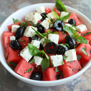 A vibrant Watermelon & Feta Salad bursting with goodness! Featuring juicy diced watermelon, creamy feta cheese cubes, and savory black olives, this refreshing dish is beautifully presented in an elegant white bowl. Garnished with aromatic fresh basil leaves and a hint of black pepper, it's a delightful mix perfect for any occasion. Experience the freshness and health benefits of Zestful Blends' creations. Our commitment to eco-friendly practices makes every bite not only delicious but also kind to our planet. Dive into wellness with every forkful!