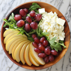 A wooden bowl brimming with our vibrant Asian Pear & Grape Salad, bursting with goodness! This refreshing delight features sliced yellow apples, crispy Asian pears, succulent red grapes, a medley of crumbled and cubed cheese, and crisp green arugula leaves. Each ingredient is meticulously arranged on a marble countertop to highlight its freshness and health benefits. Enjoy this eco-friendly masterpiece from Zestful Blends—where every bite celebrates vitality and sustainability!