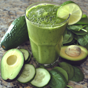 A vibrant tall glass of our refreshing Citrus Sunrise, garnished with a zesty lime slice, takes center stage on a gleaming countertop. Surrounding this burst of goodness are halves of creamy avocado, crisp cucumber slices, and fresh spinach leaves. A whole avocado and cucumber along with more lush spinach bask in the gentle glow of sunrise, showcasing the freshest ingredients packed with essential nutrients. At Zestful Blends, we celebrate nature's bounty in every sip and bite—healthy delights that are as eco-friendly as they are delicious!