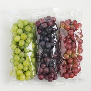 Three vibrant bundles of grapes, bursting with goodness, are artfully lined up in a row. The left bag showcases luscious green grapes, the middle bag boasts rich dark purple grapes, and the right bag features succulent red grapes. Each eco-friendly package is sealed to lock in maximum freshness and flavor. Perfect for fruit salads, juices, snacks, smoothies, whole fruit packs, or desserts—our meticulously selected produce embodies the vitality and freshness that Zestful Blends is known for. Savory delight straight from nature to your table!